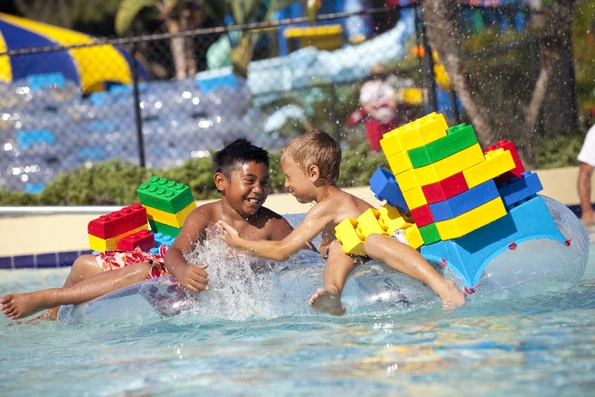 Kids float on oversized LEGOs in a water park pool.