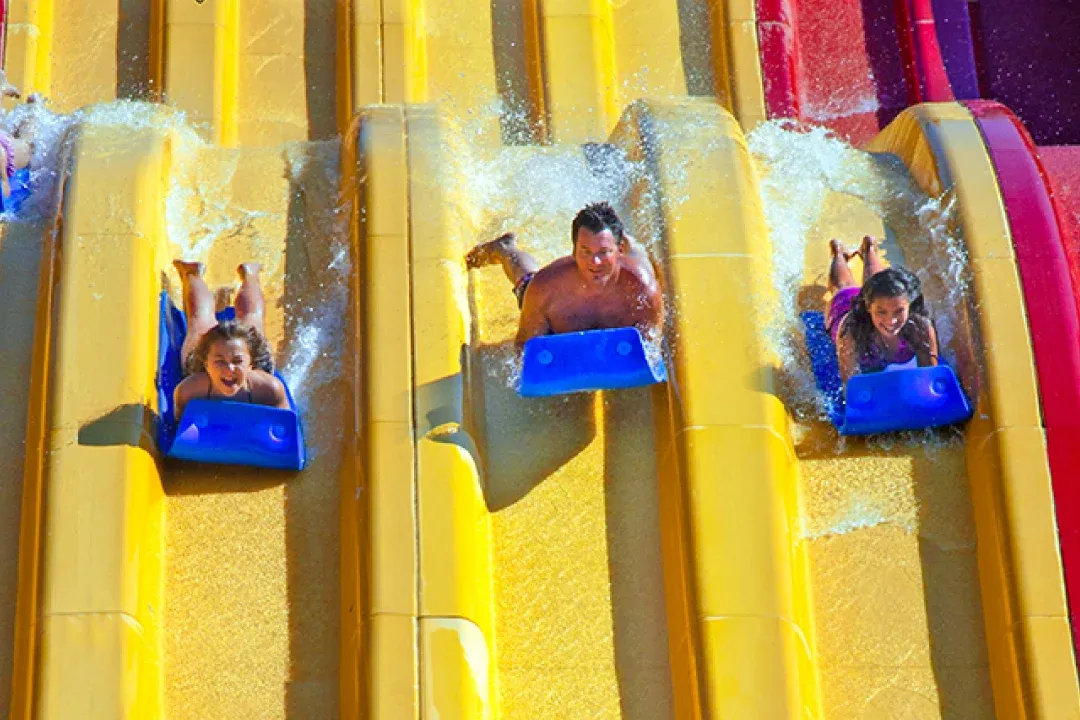 Three people go down a yellow water slide at Raging Waters San Dimas.