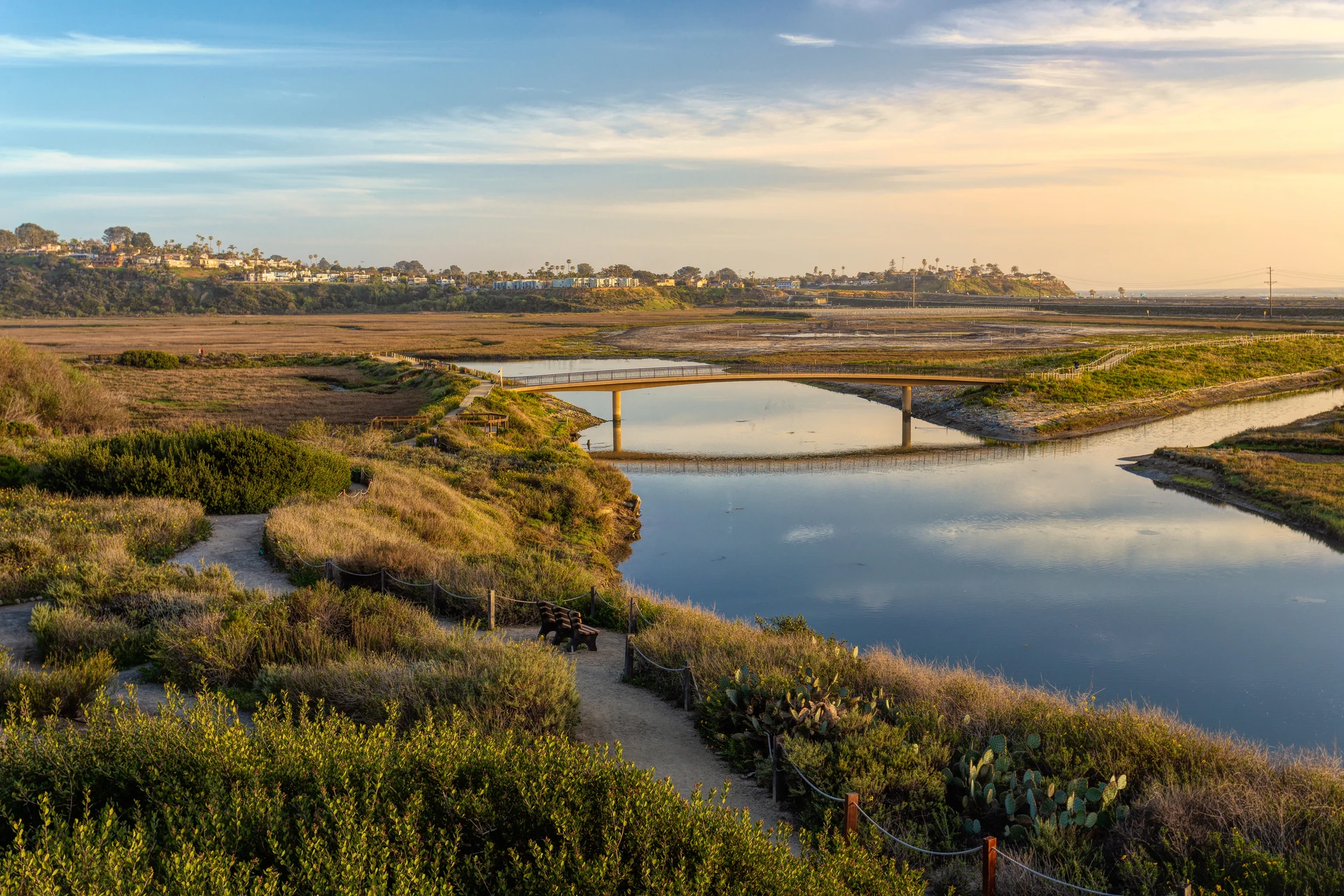 Trails with benches and a bridge crossing the lagoon at golden hour.