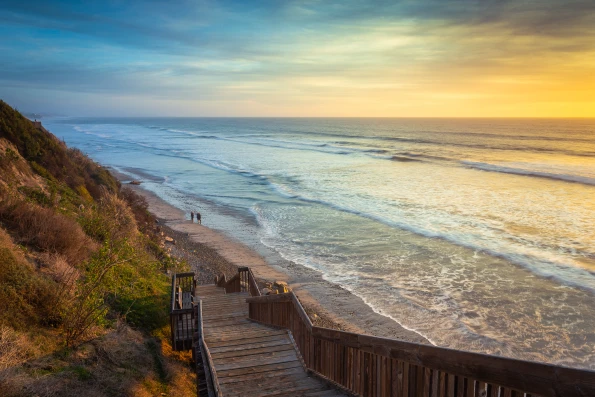 Two people walking along the shoreline at San Elijo State Beach during sunset.