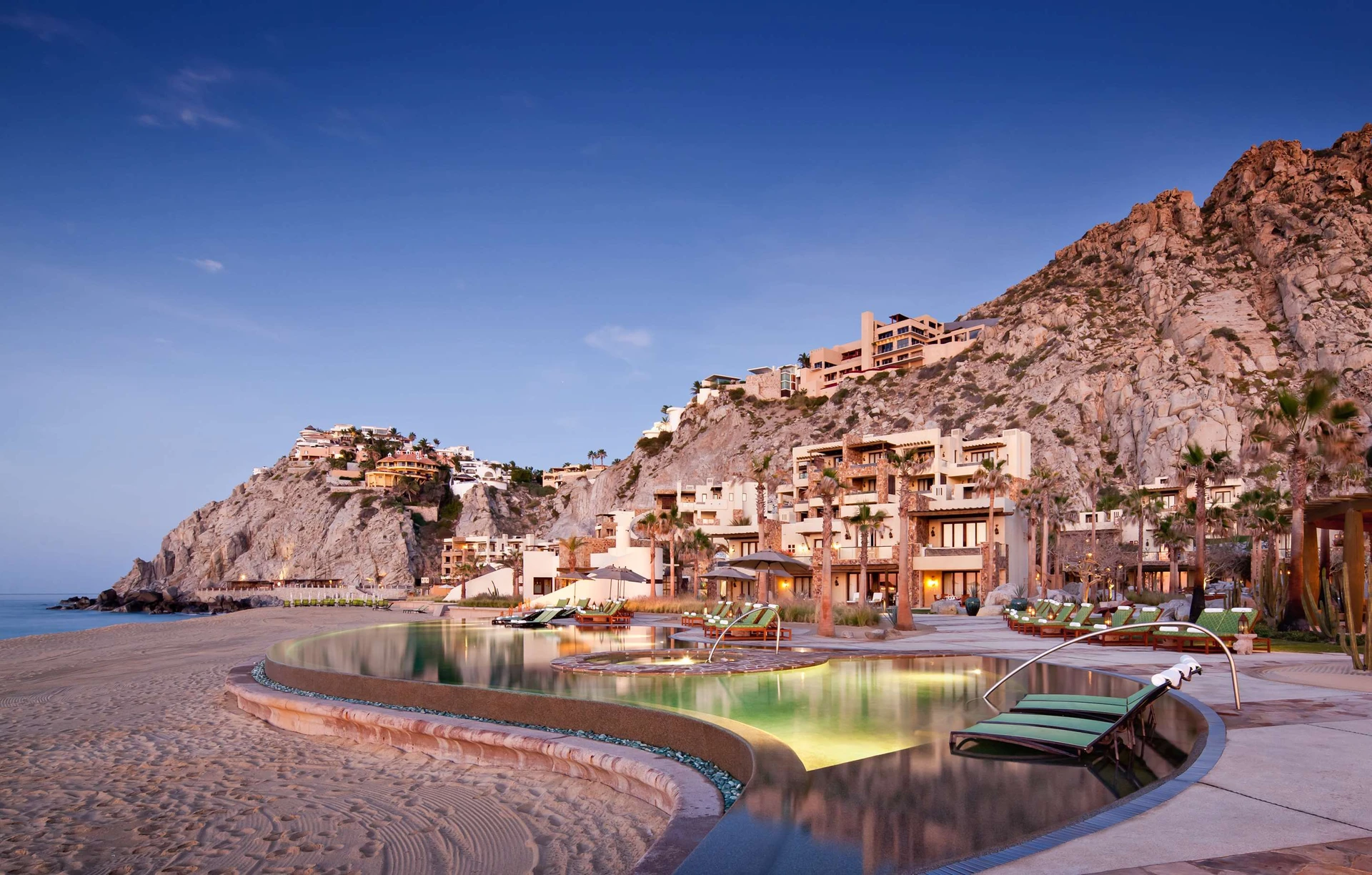 The Waldorf Astoria Cabo beachfront pool lit up at golden hour.