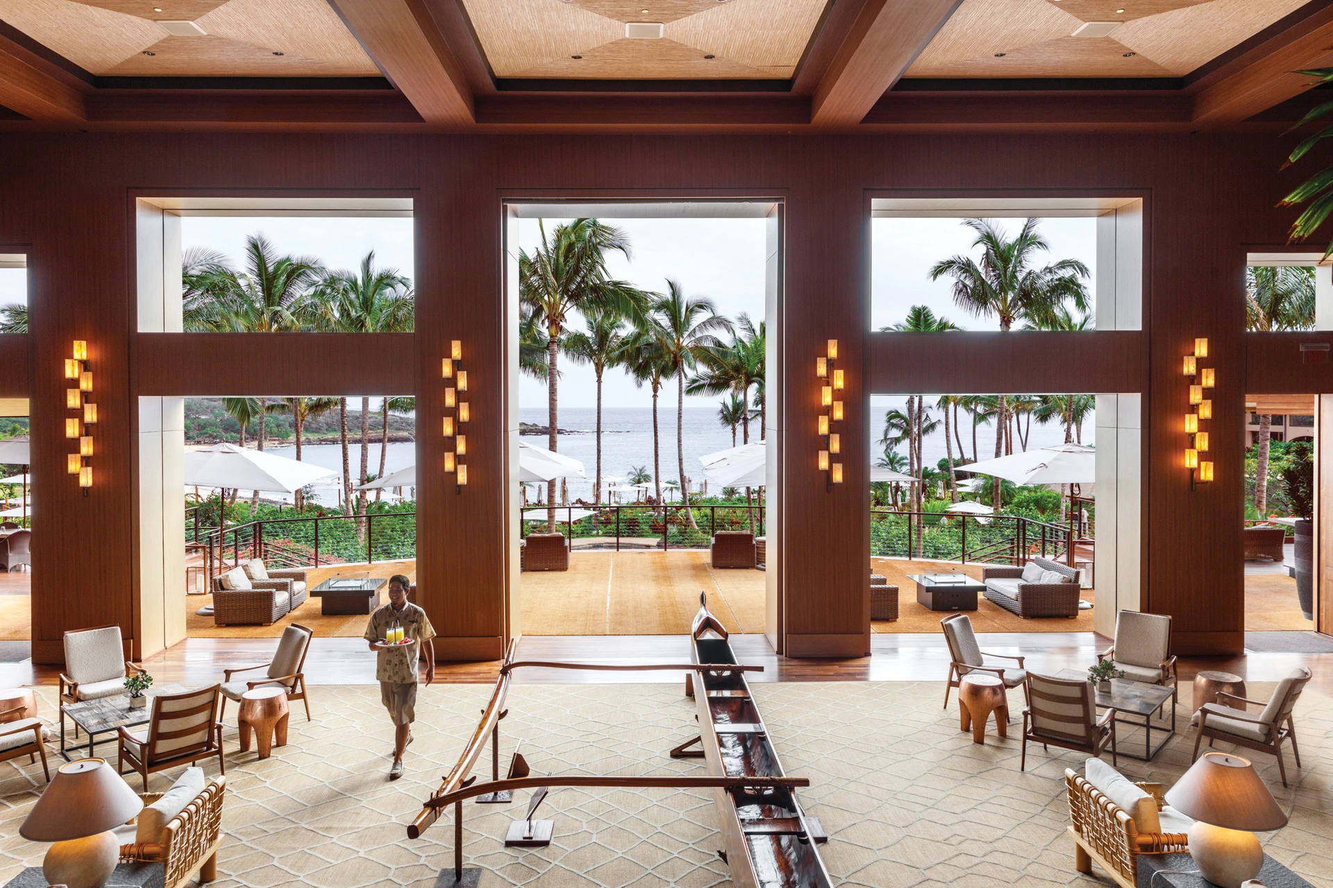 A server walks thorugh the Four Seasons Lanai hotel lobby with drinks on a tray.