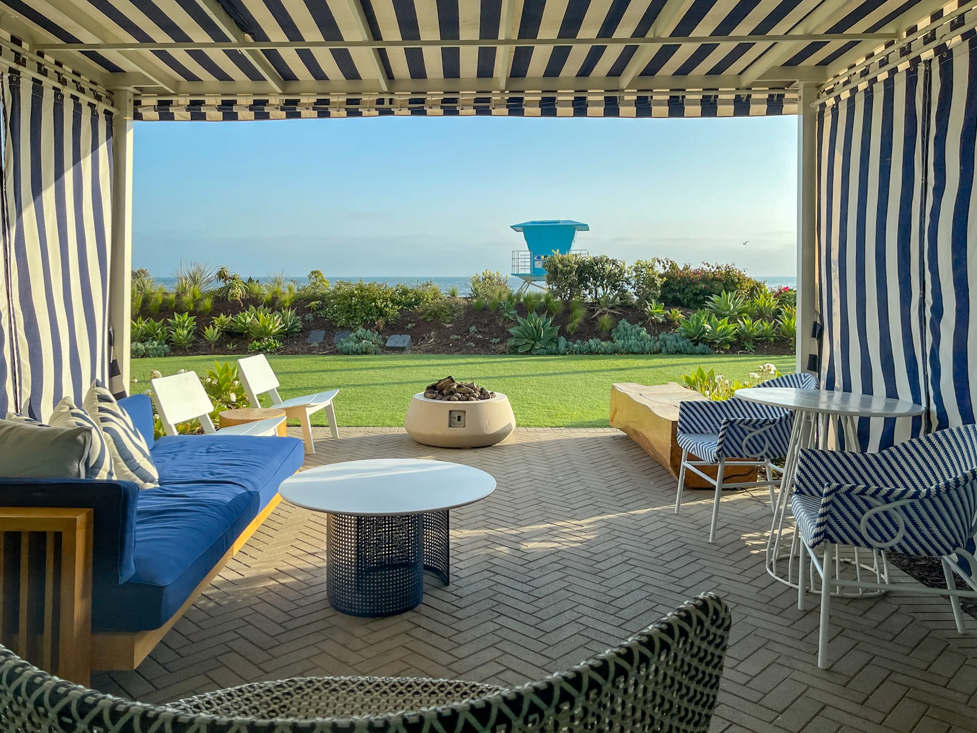 The furnished covered patio area with sofa and chairs and fire pit looking toward the ocean.