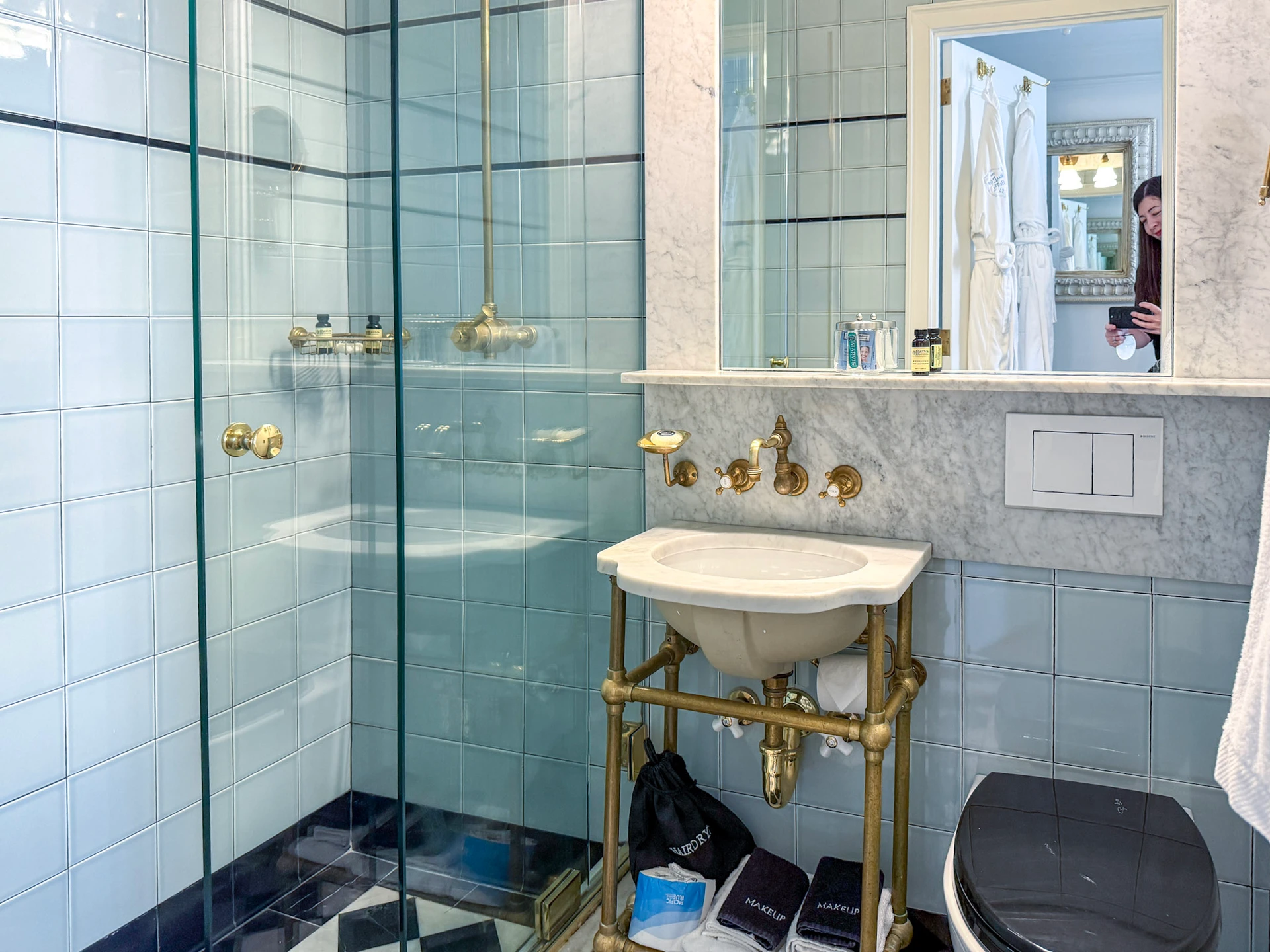 My petite bathroom with walk-in shower, small standalone sink, toilet, minimal shelving.