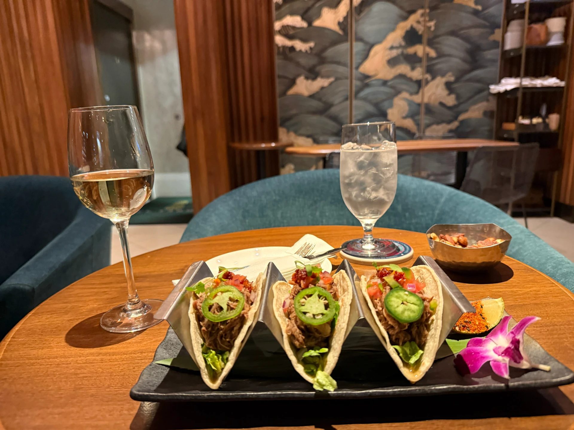 Three short rib tacos presented on a table at El Ta’Koy with a class of white wine.