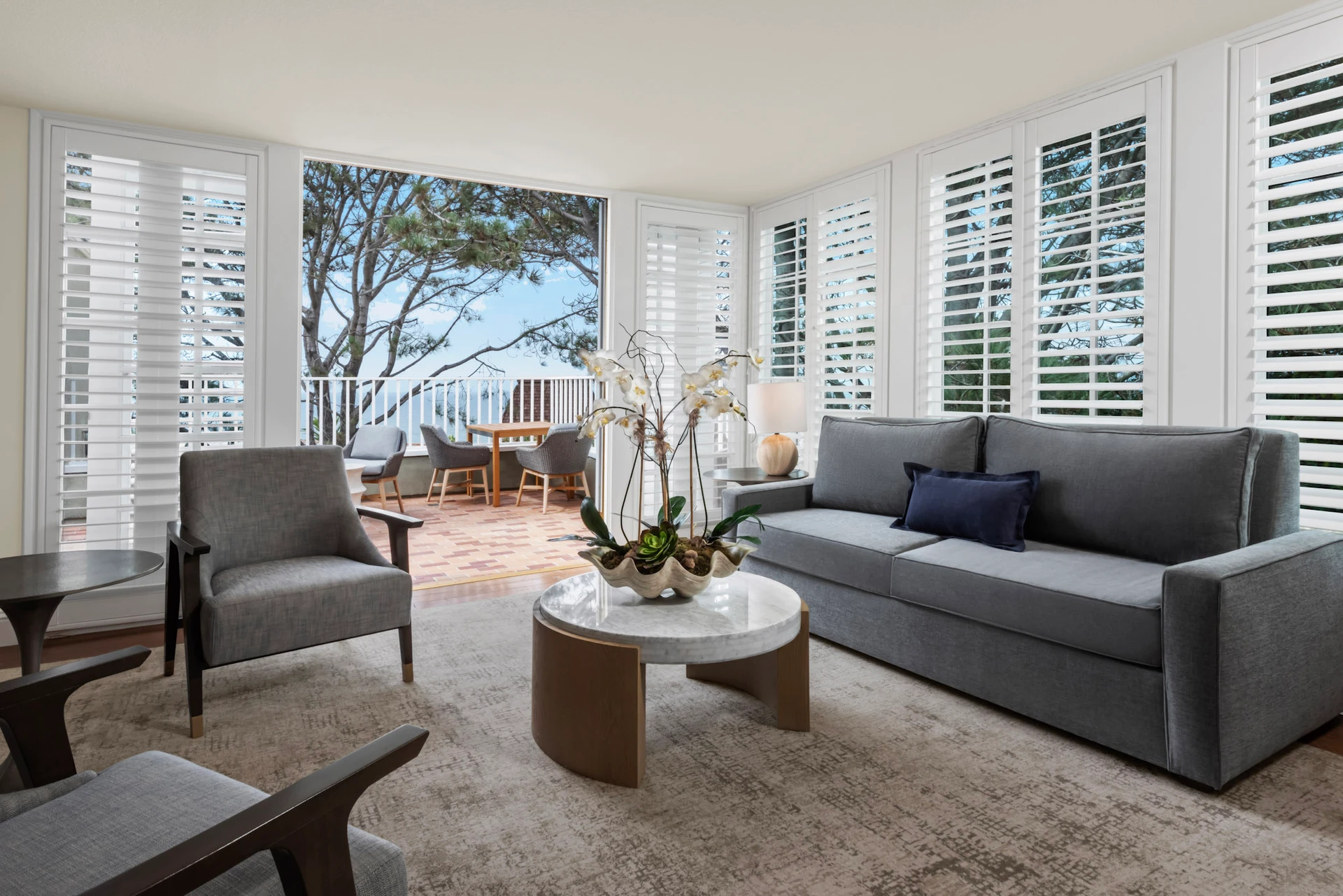 The living room of the Del Mar Suite with balcony showing ocean view through trees.
