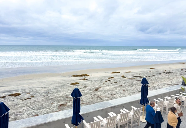 The oceanfront deck with lounge chairs and umbrellas at Del Mar Beach Hotel, looking out over the sand and surf in Del Mar
