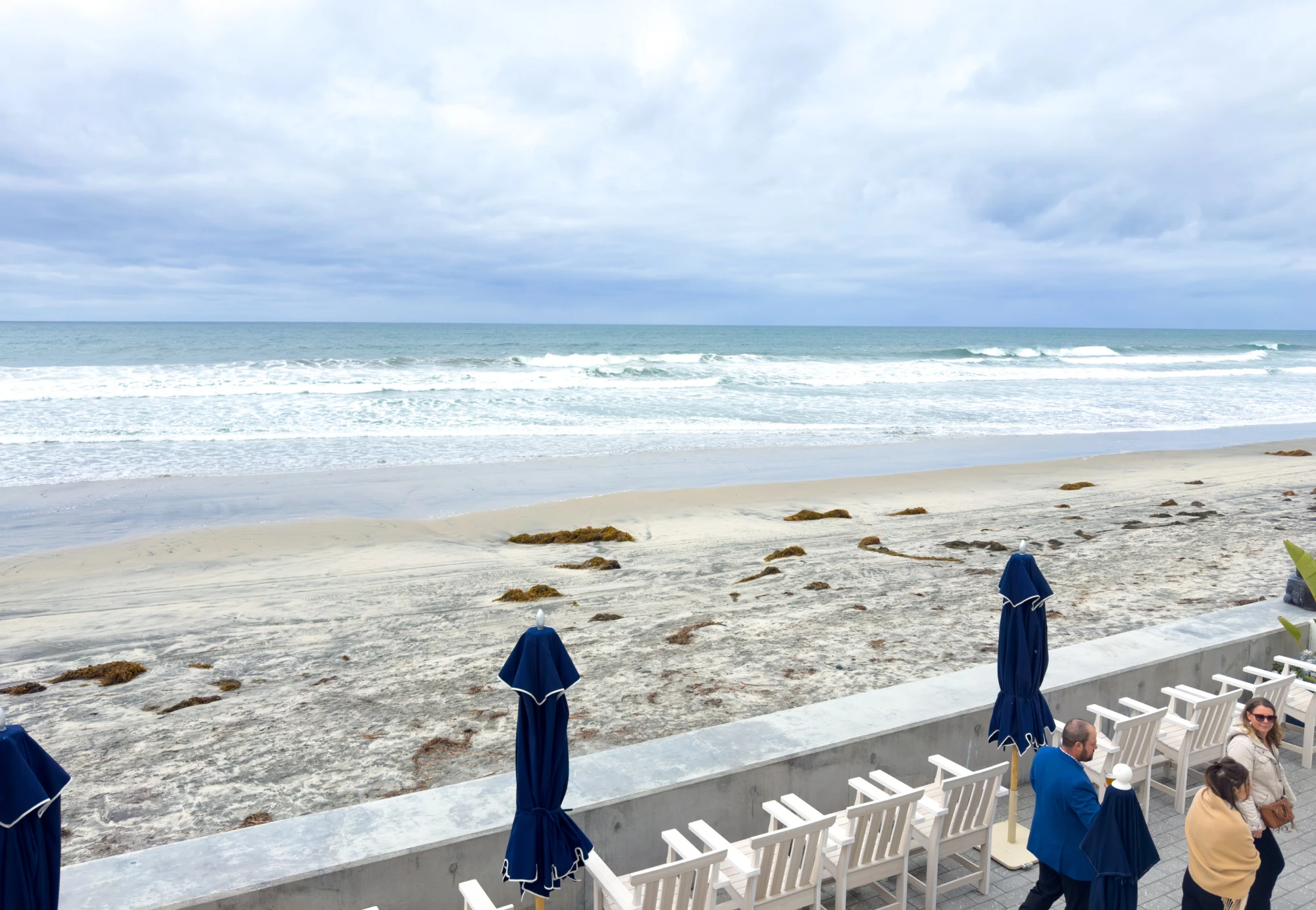 The oceanfront deck with lounge chairs and umbrellas at Del Mar Beach Hotel, looking out over the sand and surf in Del Mar