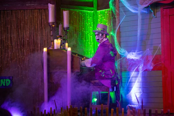 A performer in skeleton face paint and a purple costume plays a candlelit organ surrounded by fog and cobwebs at HalGLOWeen.