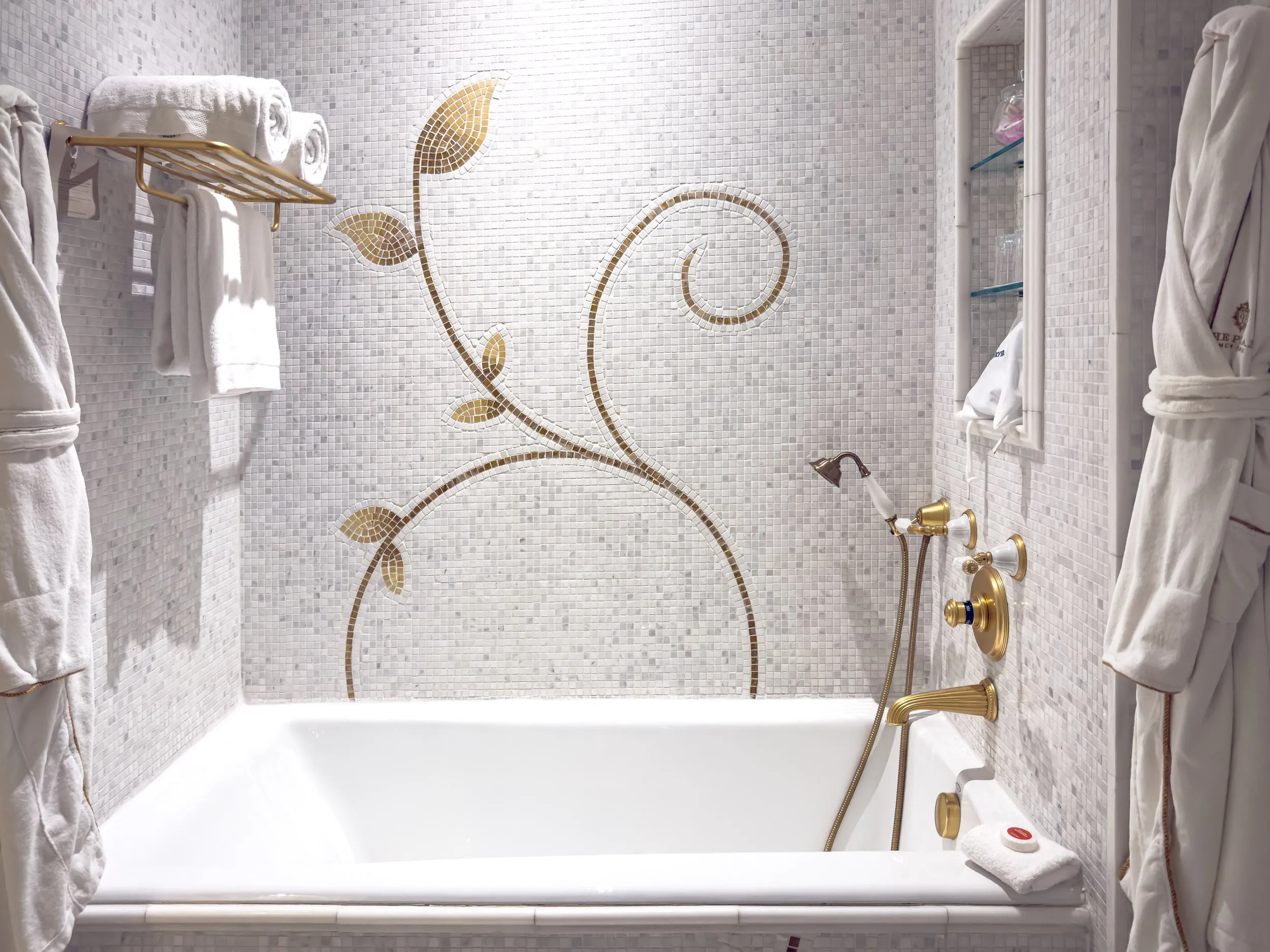 Marble bathroom with soaking tub, gold fixtures and hanging robes at The Plaza Hotel New York