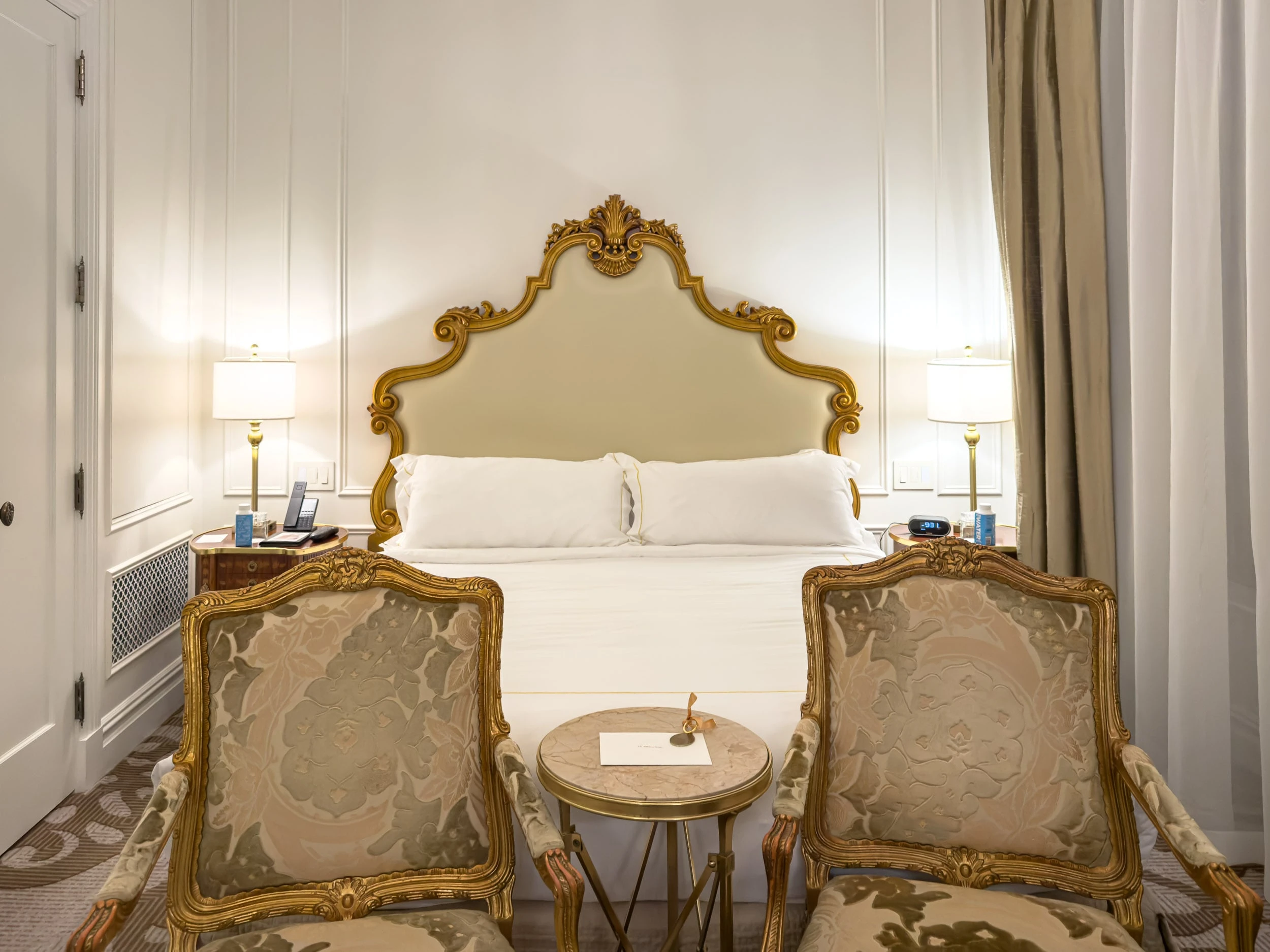 Guest room bed with carved gilt headboard and gold armchairs at The Plaza Hotel New York