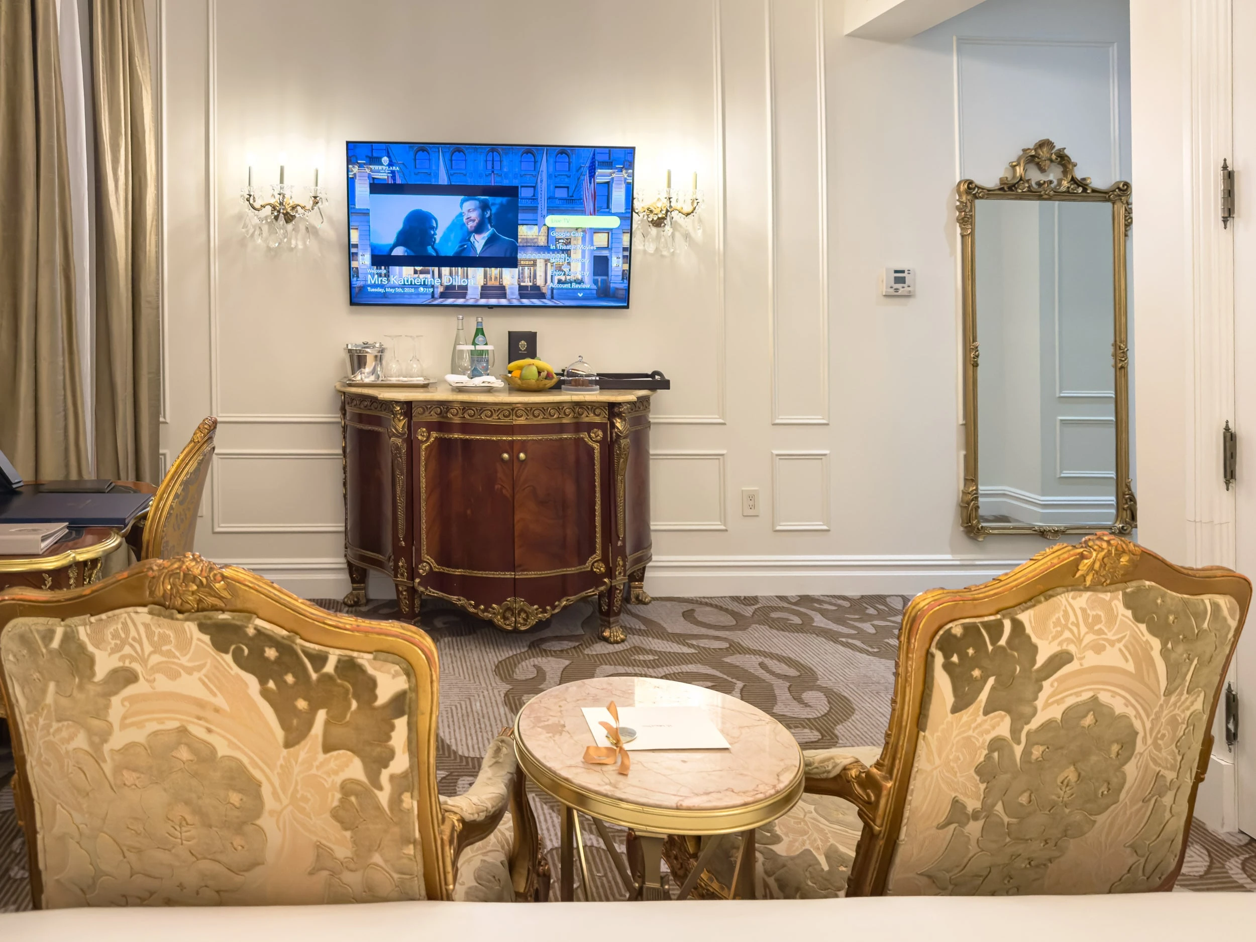 Guest room sitting area with wall-mounted television and gilt mirror at The Plaza Hotel New York