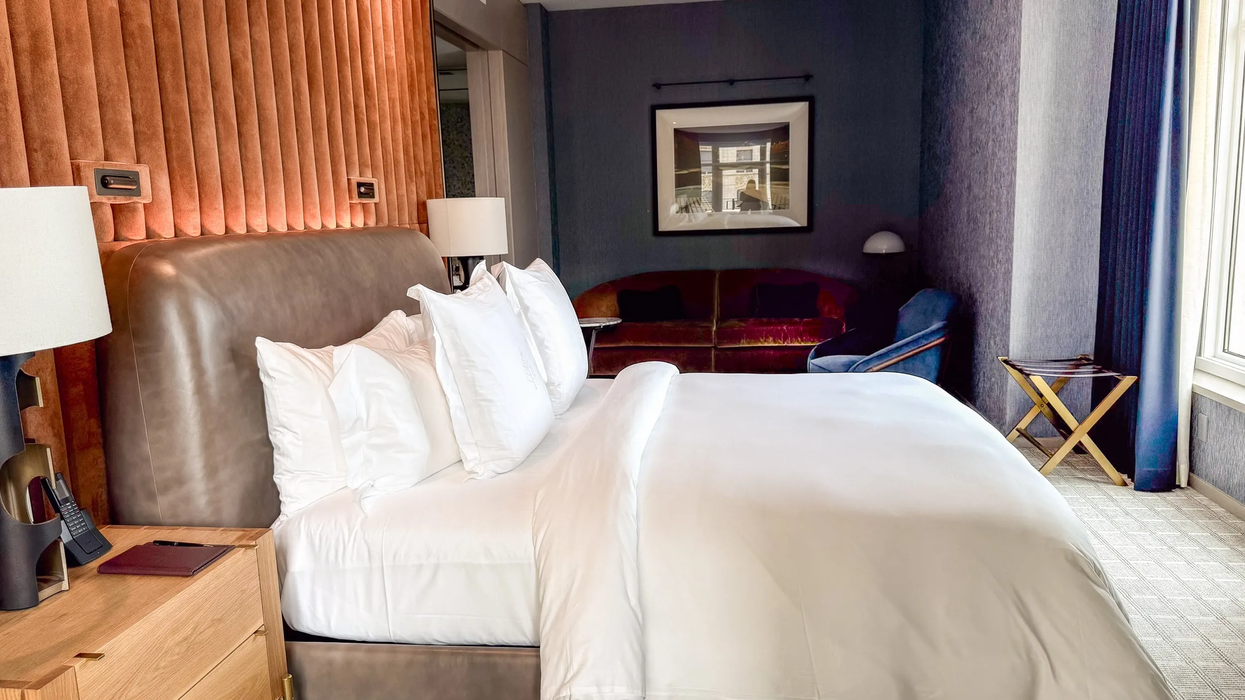 The Gotham Suite bedroom, with a sofa, blue walls, and a plush rust-colored headboard.
