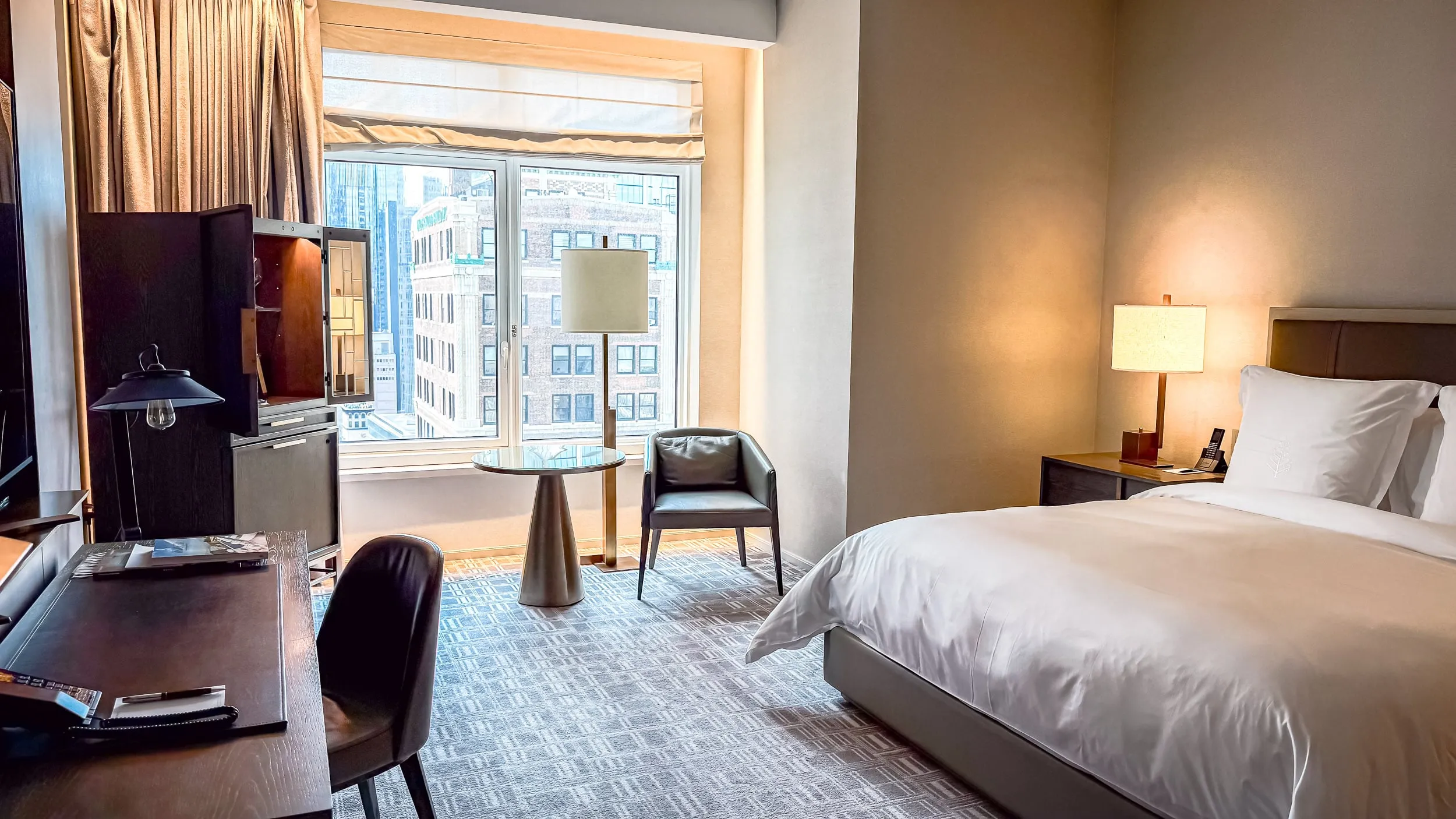 The bed, bar cabinet, desk, and view in a Manhattan Room at Four Seasons Hotel New York Downtown.