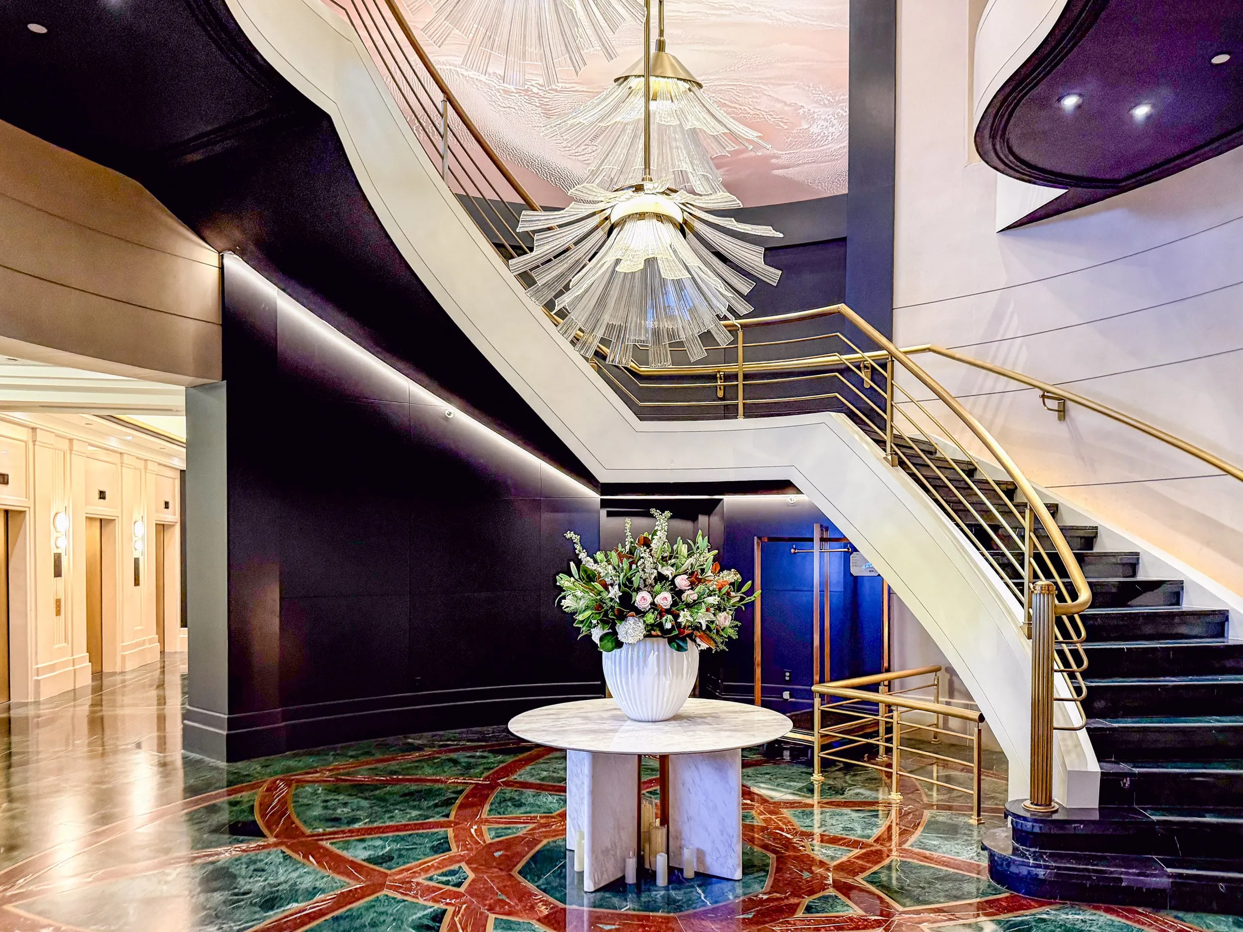 A flower arrangement sits on a marble table below a huge glass art deco chandelier at Sofitel New York City.