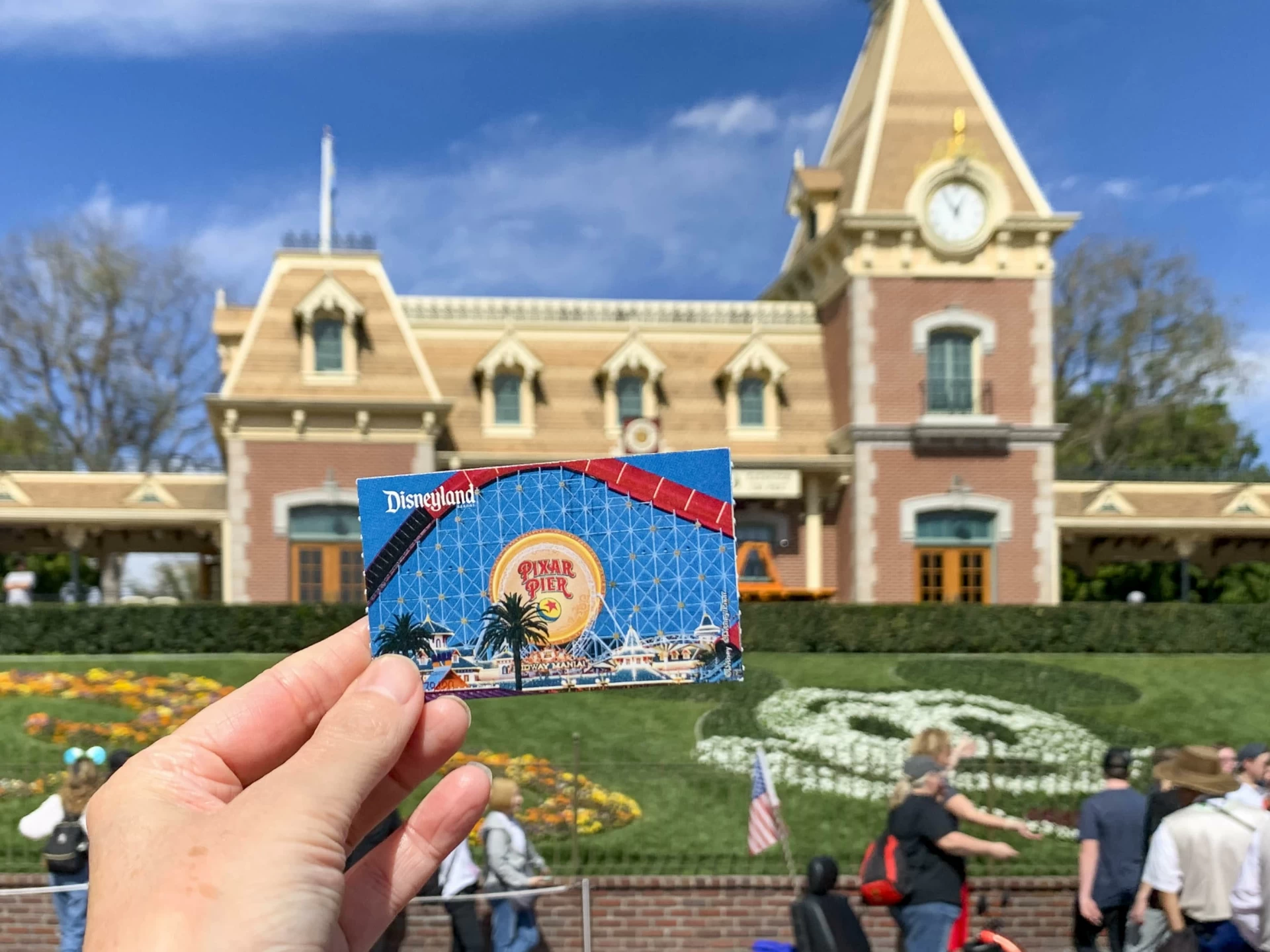 A printed Disney California ticket held up against the Main Street U.S.A. train station facade.