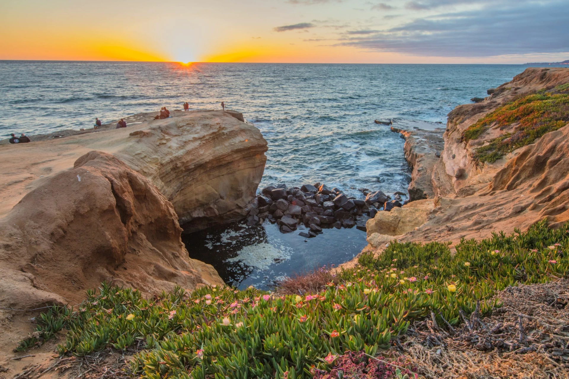 People sit on bluffs during sunset at Sunset Cliffs in Ocean Beach San Diego.