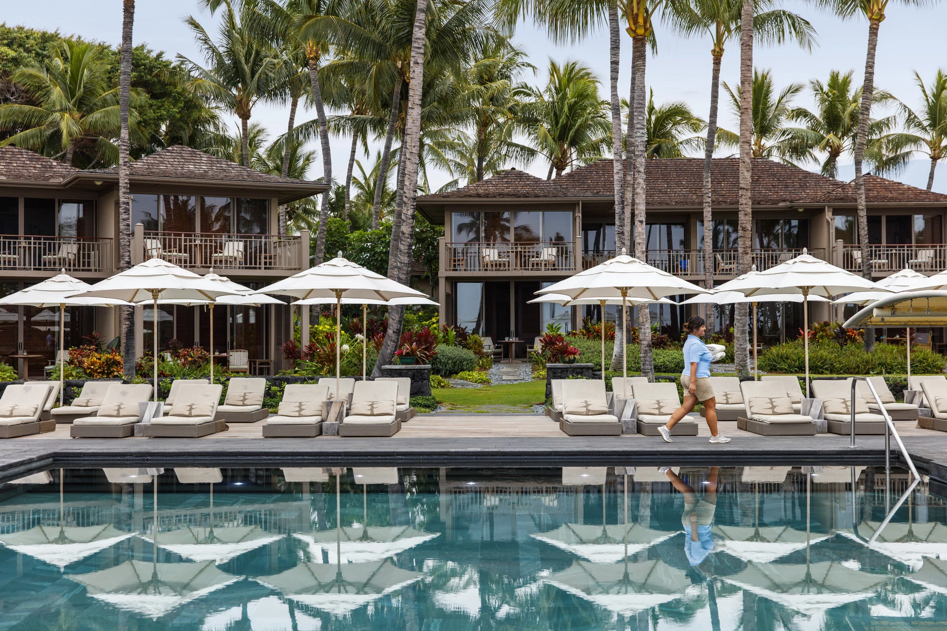 A pool attendant carries towels past lounge chairs at the swimming pool.