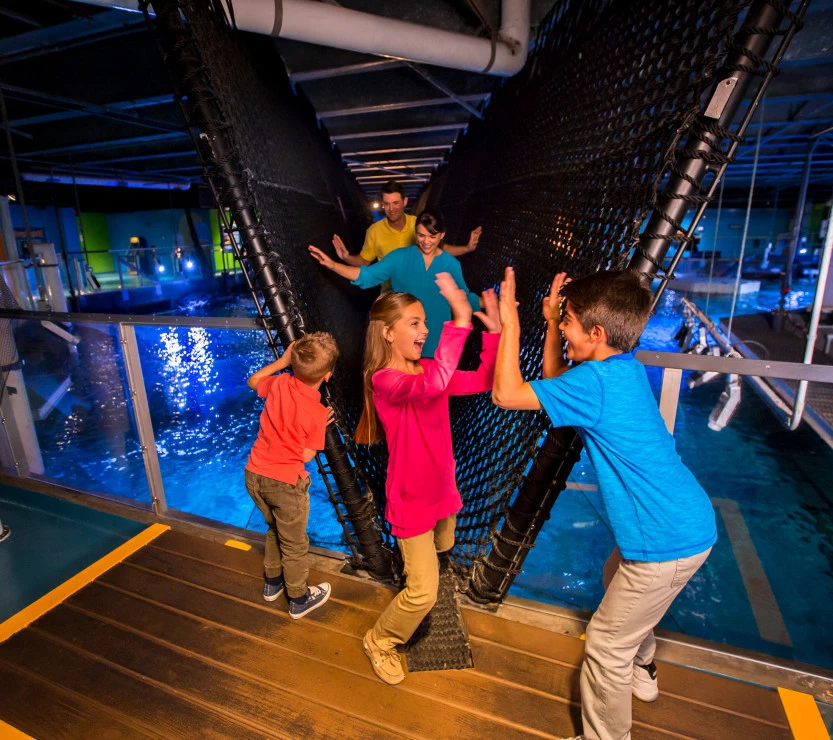 A family crosses a rope bridge over water.